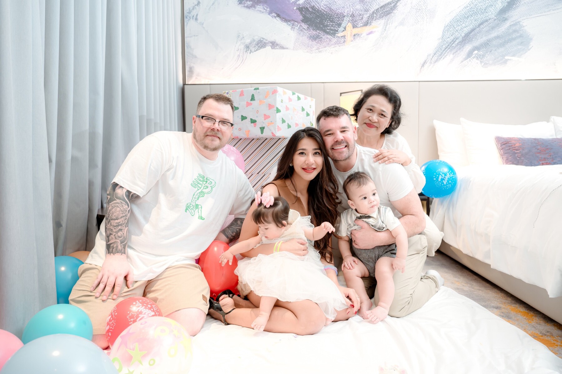 Parents, brother, and family with twins on bed with balloons
