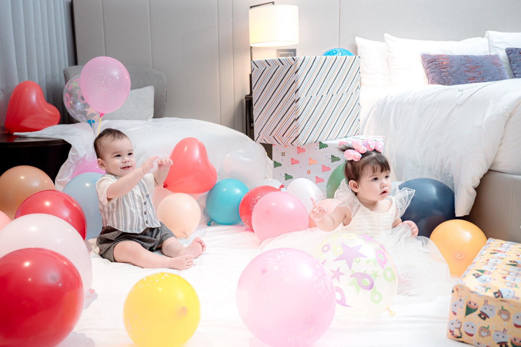 Twins sitting on bed playing with balloons
